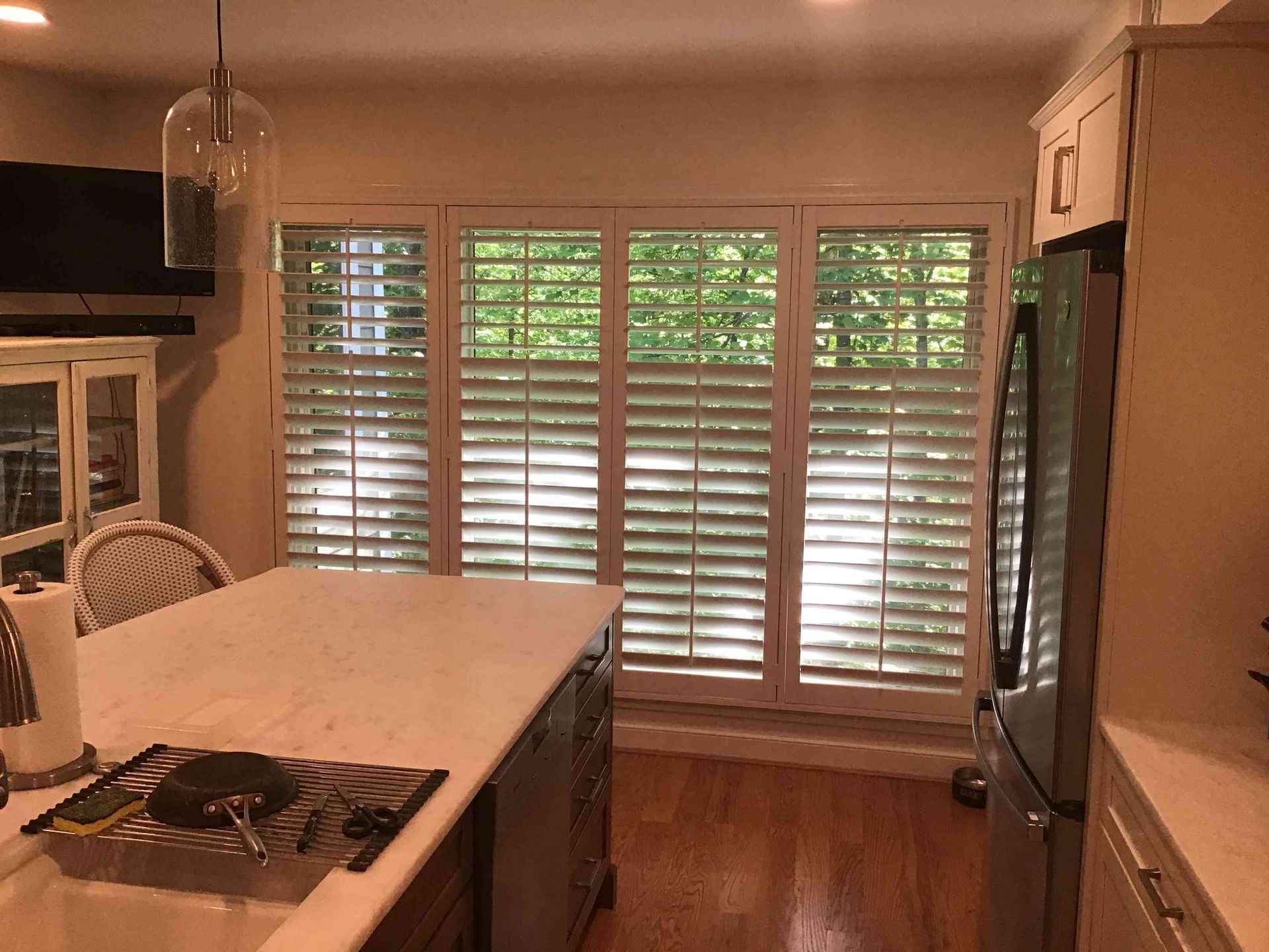 Kitchen with island cooktop and large windows covered by white shutters.