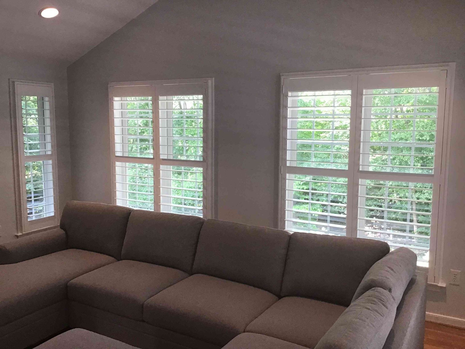 Living room with a brown sectional sofa and three large windows with white blinds