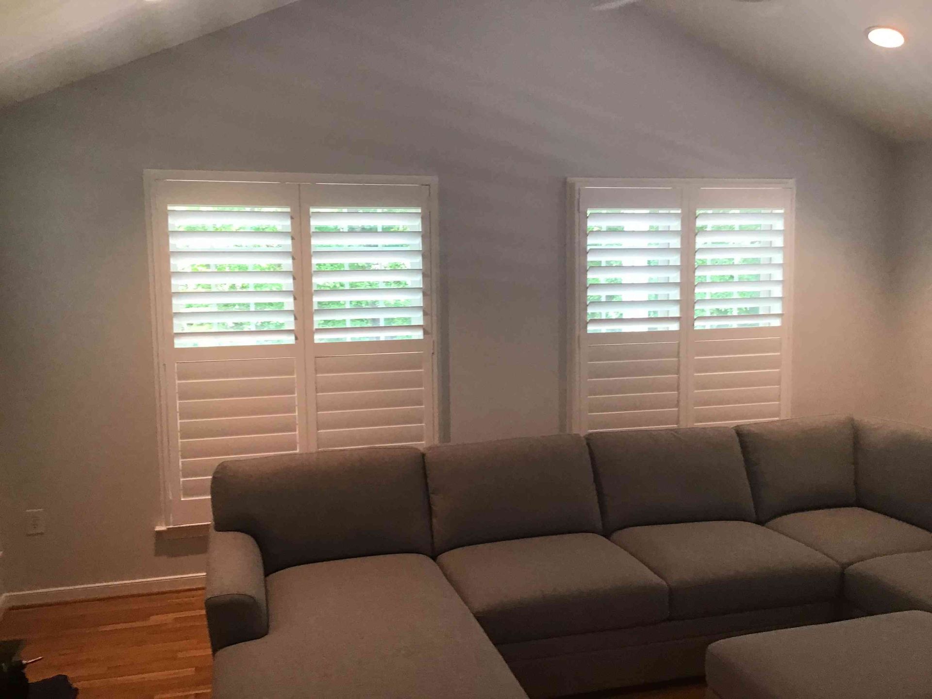 Living room with gray sectional sofa, white plantation shutters, and sloped ceiling with recessed lights