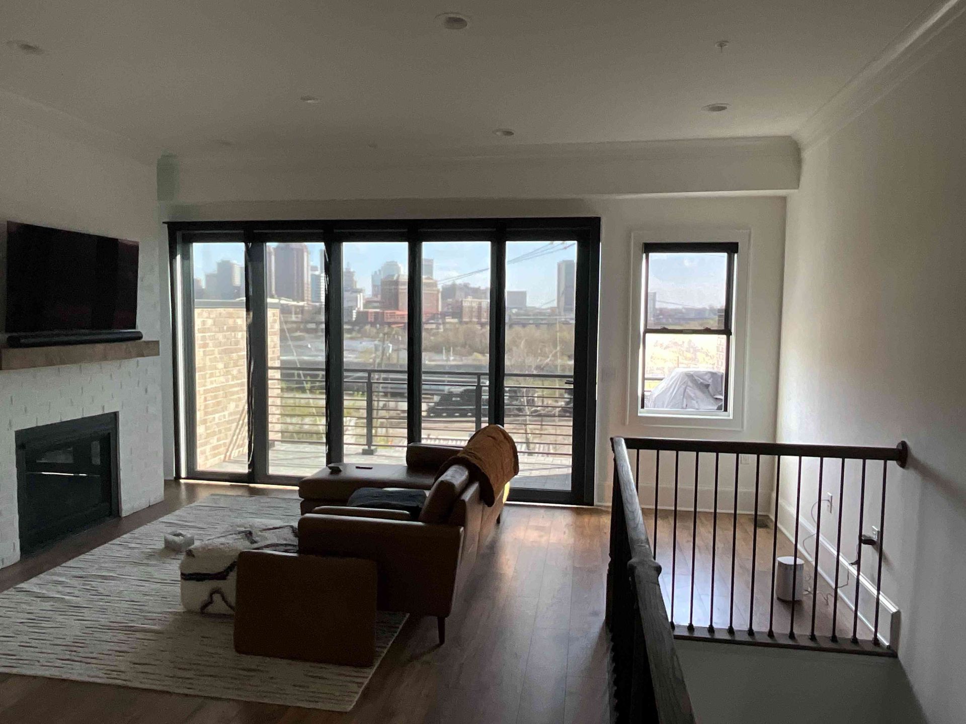 Modern living room with fireplace, armchair, rug, and large windows overlooking a city skyline