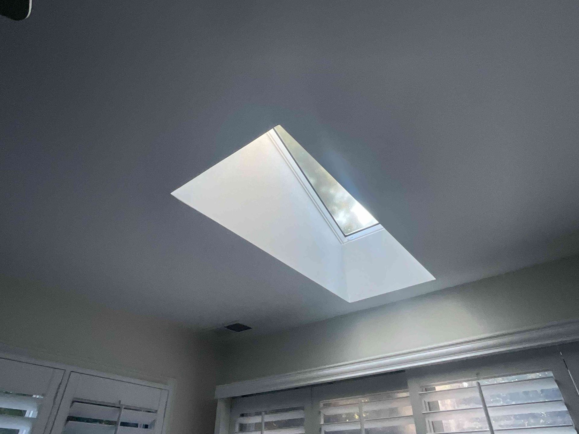 Bathroom ceiling with a rectangular skylight letting in daylight above a window and blinds