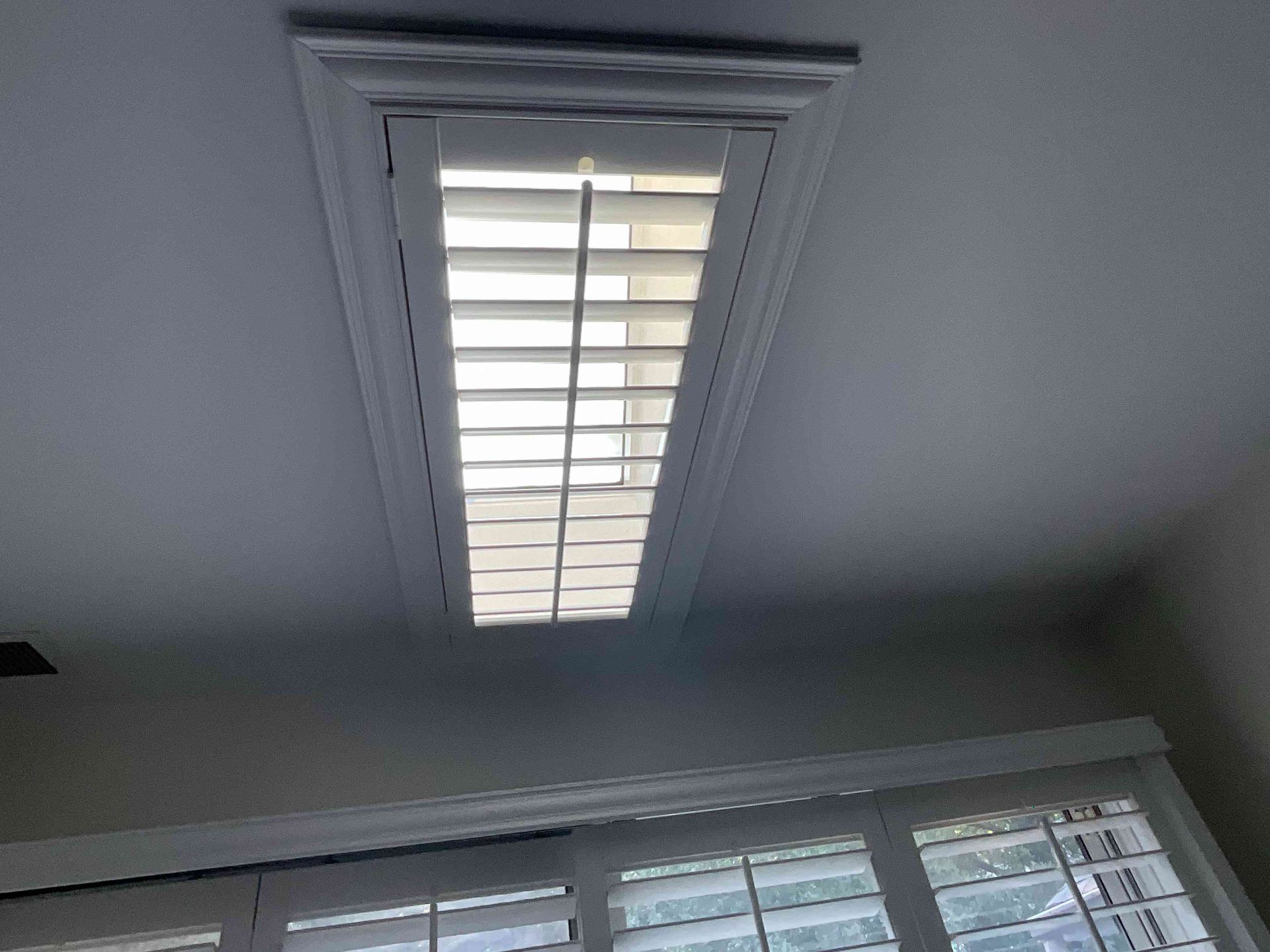 Ceiling skylight with white shutters above a row of windows in a gray room