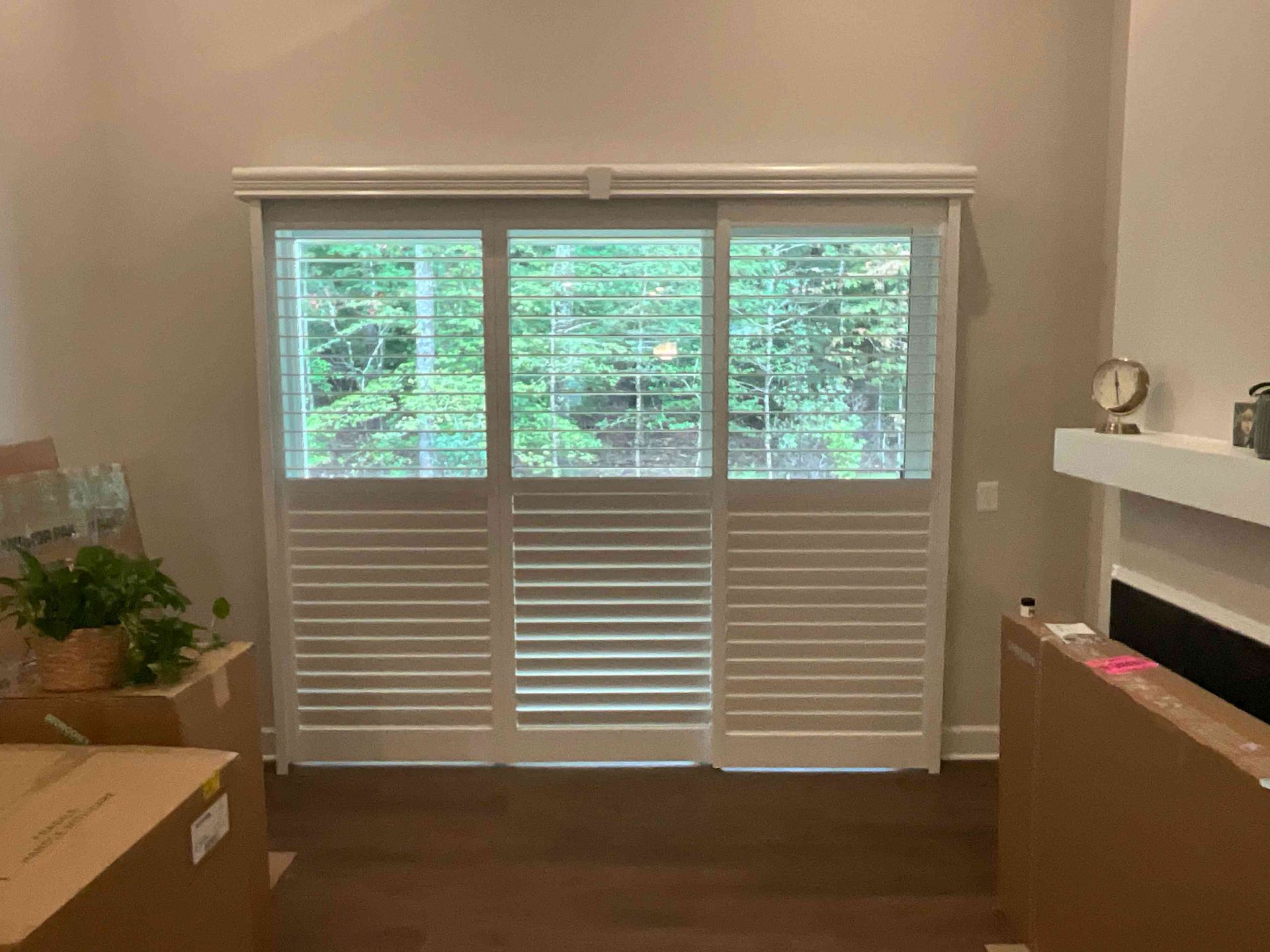 Living room with large window shutters, dark wood floor, and a fireplace mantel on the right