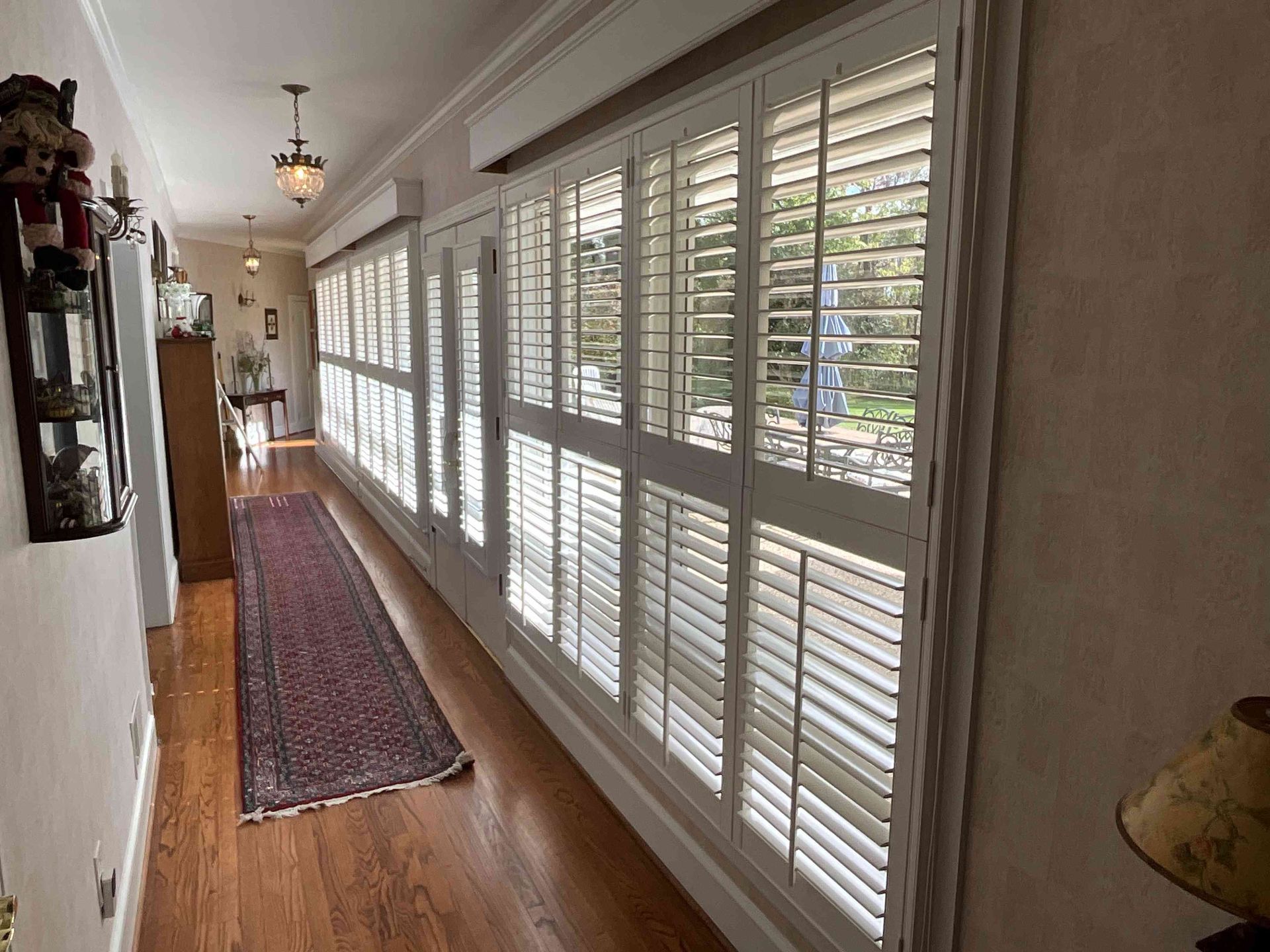 Long hallway with hardwood floor, long rug, and large windows with white shutters along one side