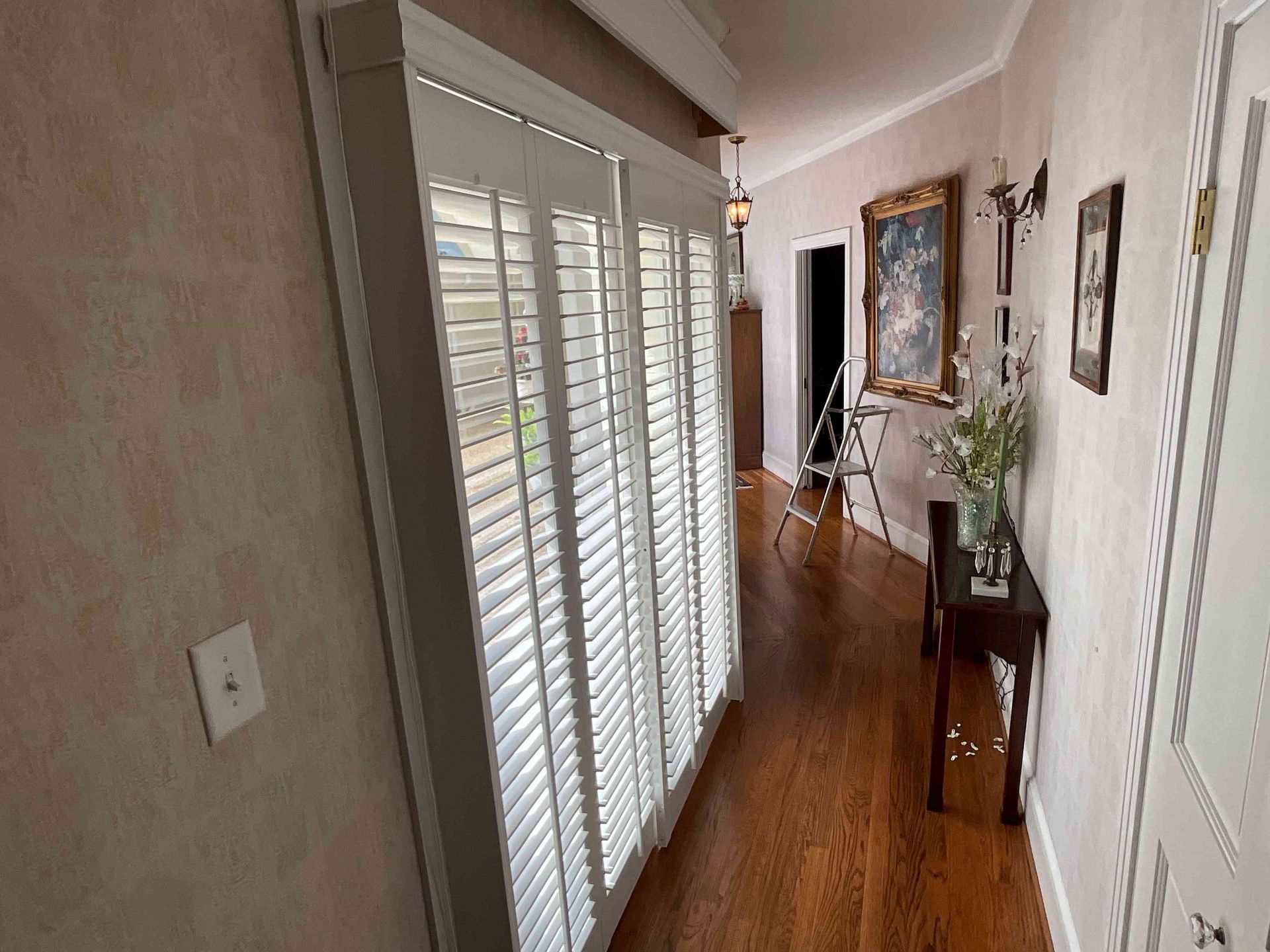Hallway with white shuttered doors, wood floor, side table, and framed wall art.