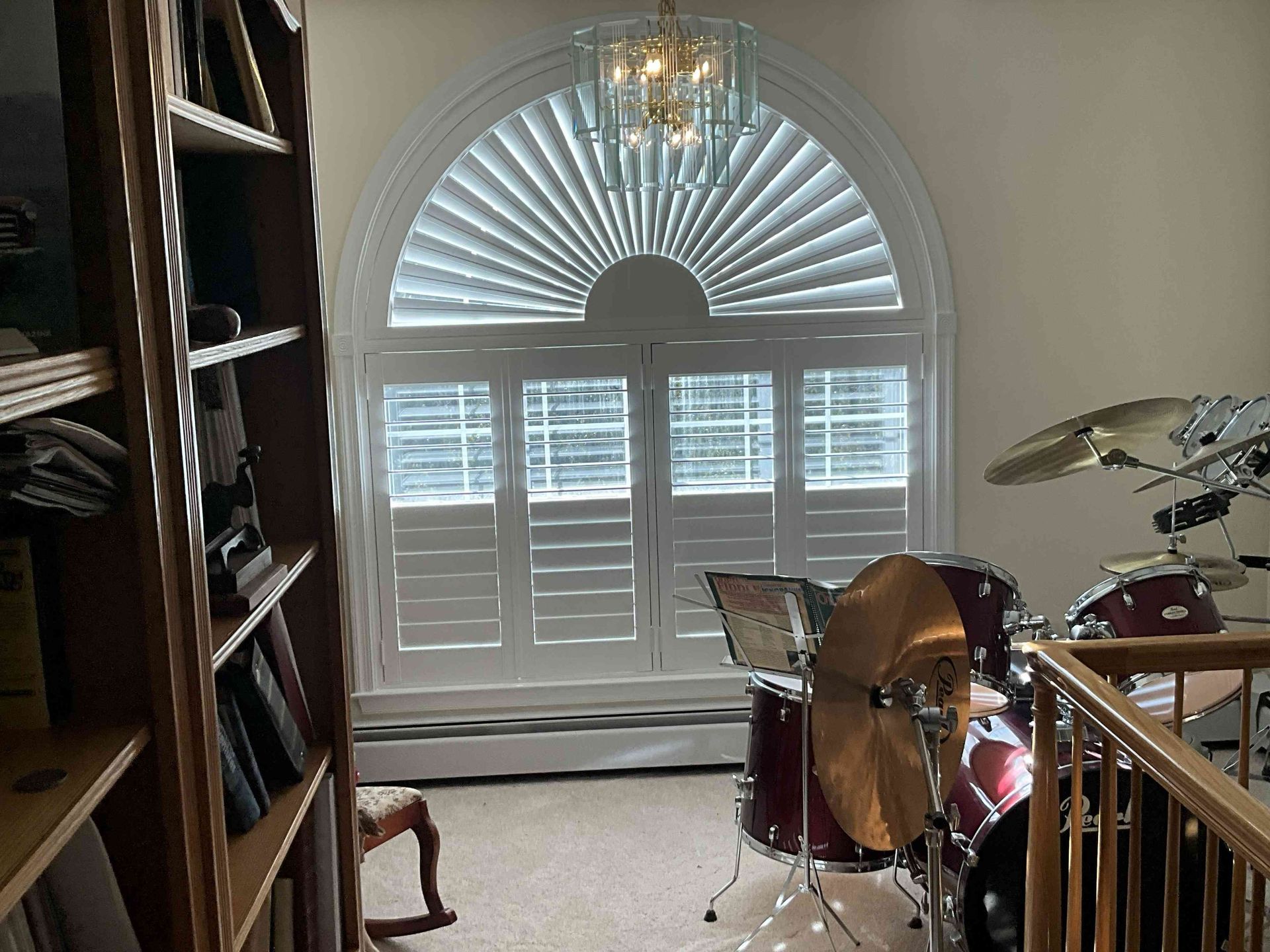 Living room with a drum set near a large arched window and bookshelf on the left