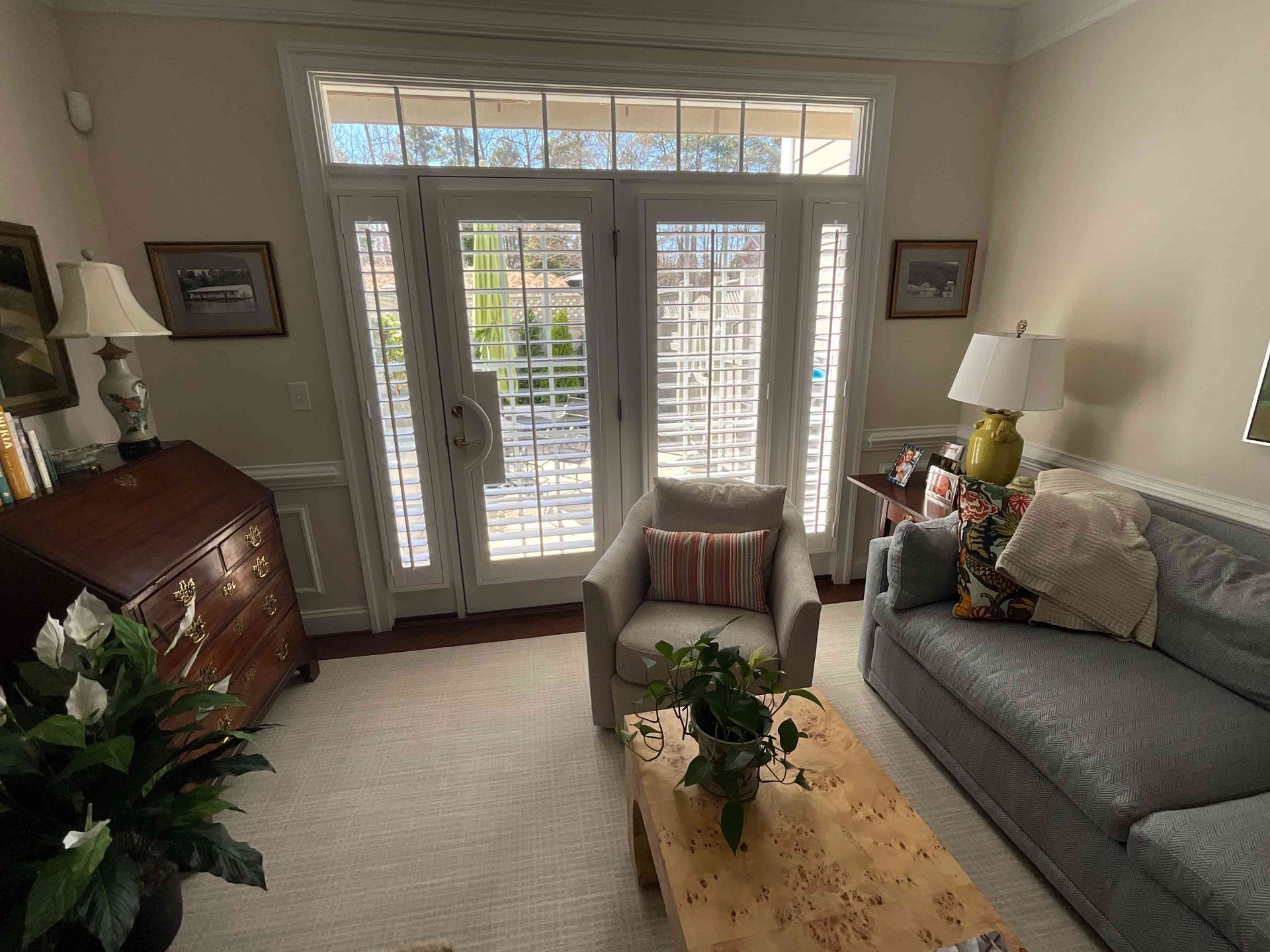 Bright living room with gray sofa, wooden coffee table, plants, and French doors with sunlight.