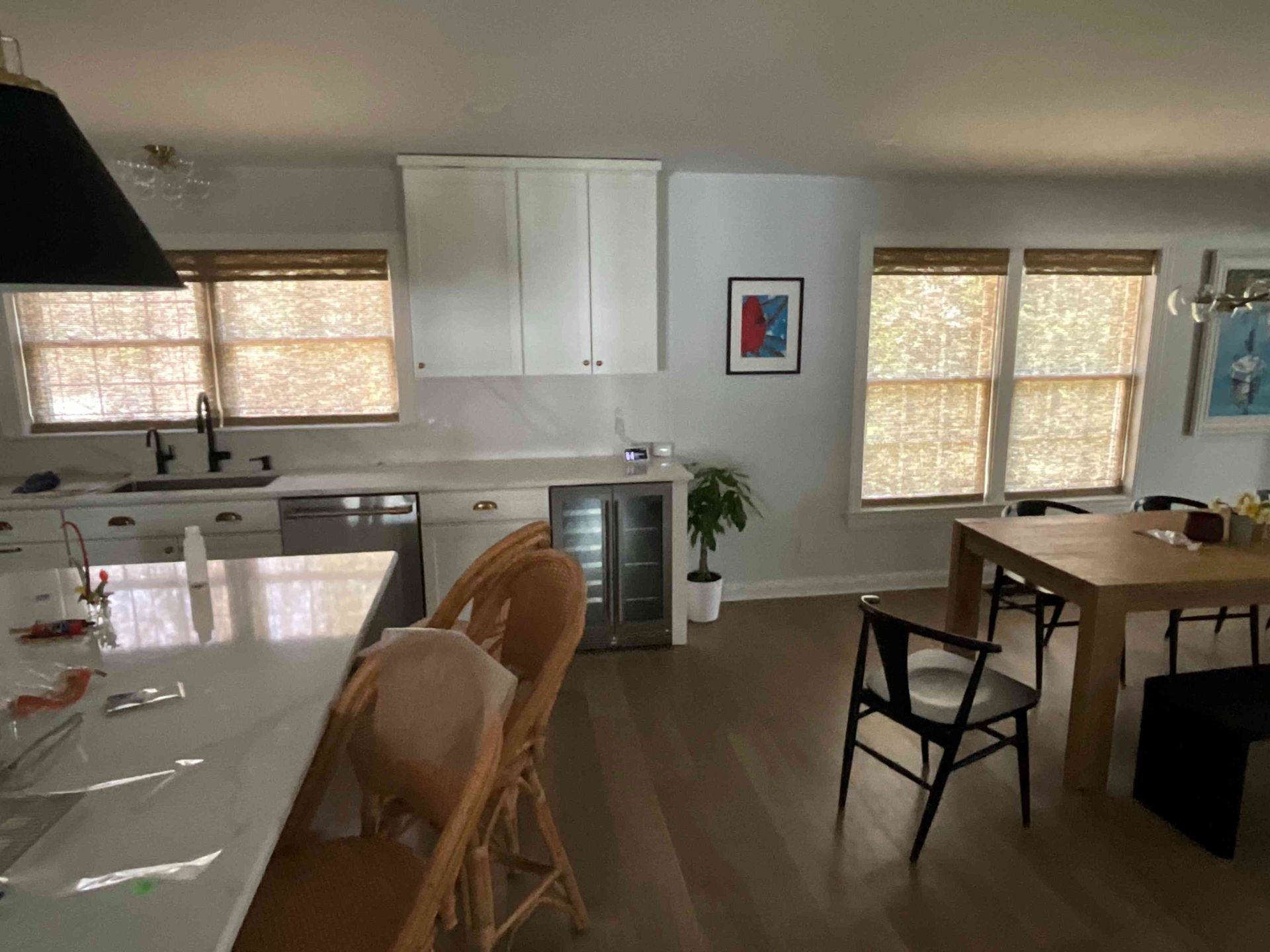 Bright kitchen and dining area with white cabinets, wood floors, woven chairs, and a table by two windows