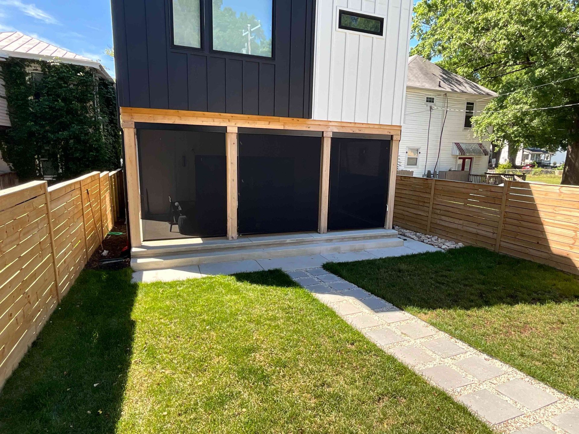 Backyard with lawn, stone path, wooden fence, and a modern house with three open garage bays.