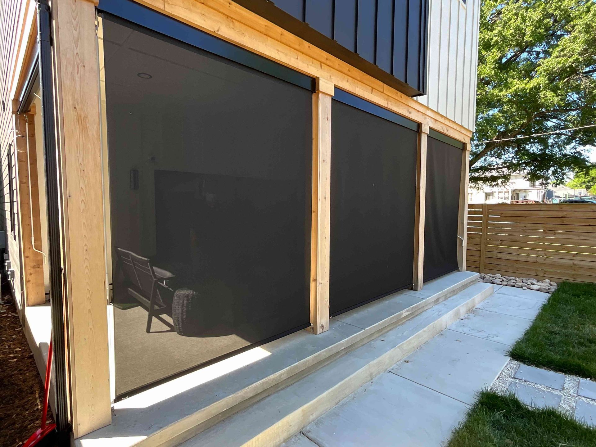 Screened porch with black mesh panels and wooden posts beside a concrete patio and steps