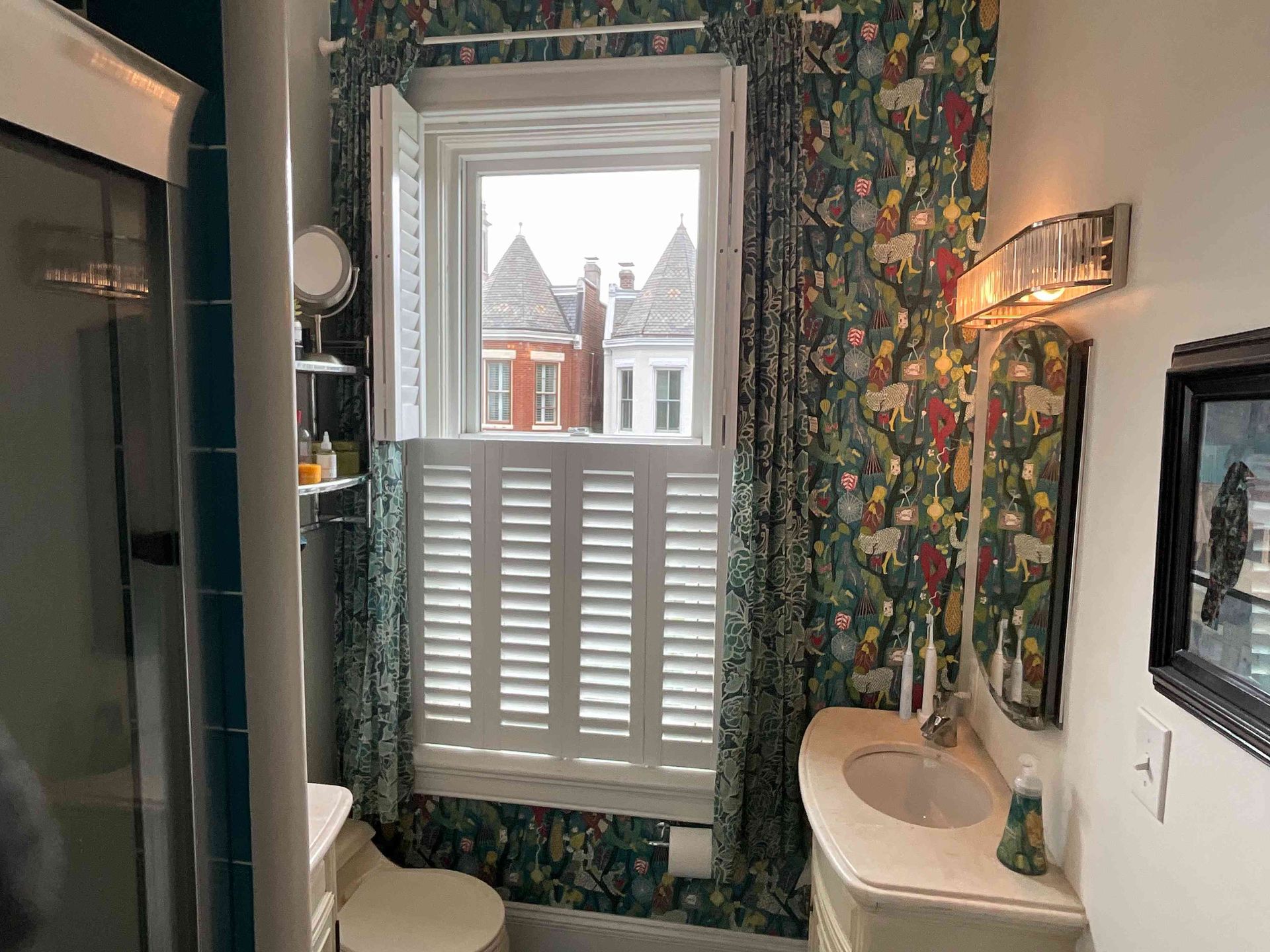 Bathroom with floral wallpaper, a sink, and a window with white shutters overlooking snowy houses