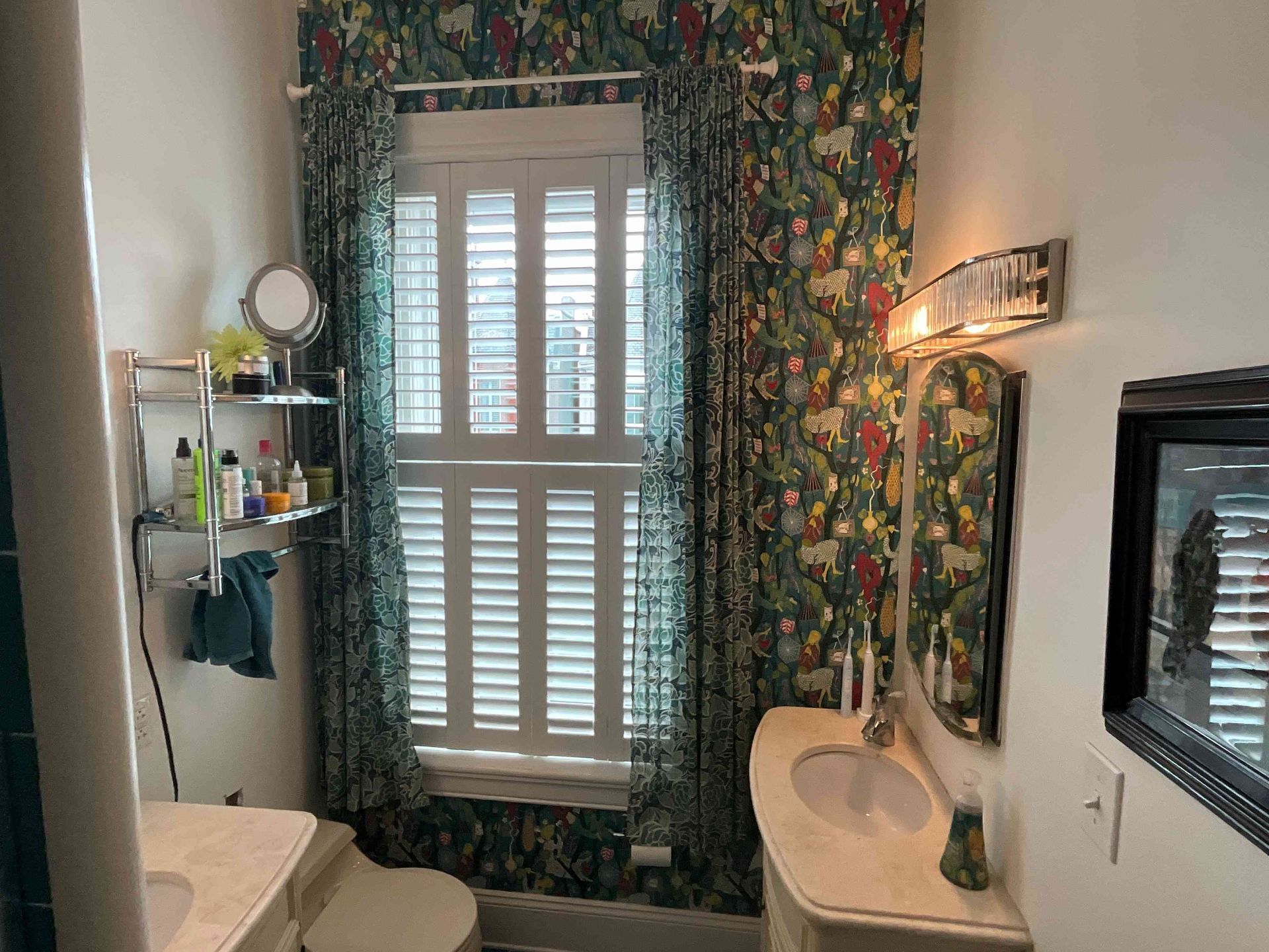 Bathroom with floral wallpaper, twin sinks, and a window with white shutters.
