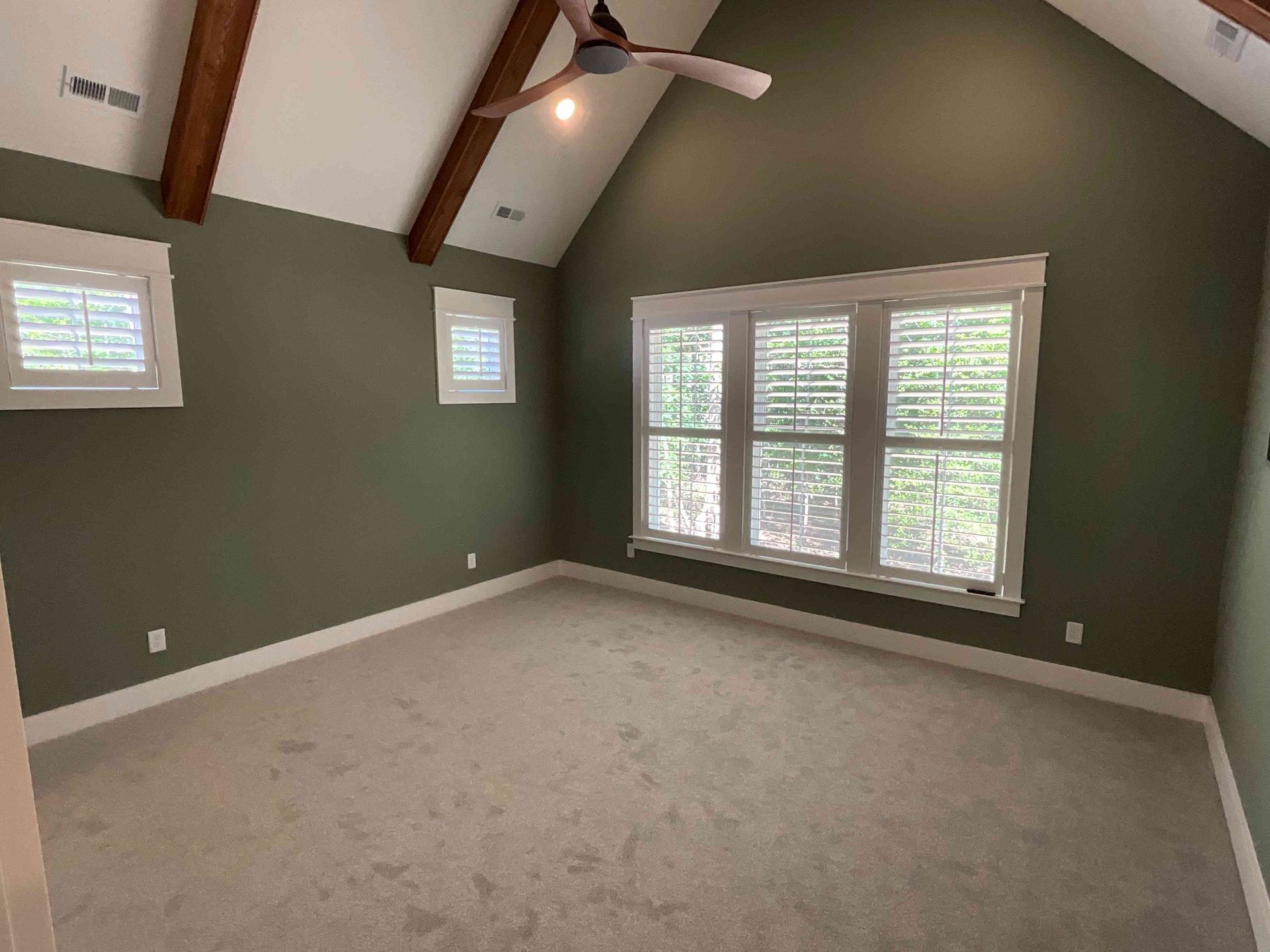 Empty bedroom with green walls, vaulted ceiling, carpet, and large windows with white trim.