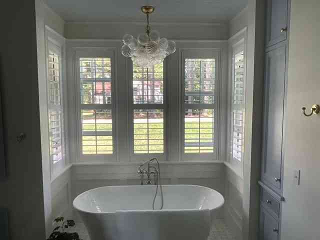 Bright bathroom with a freestanding tub before tall windows and a chandelier