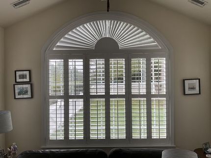 Living room window with white plantation shutters and fanlight arch, flanked by framed pictures