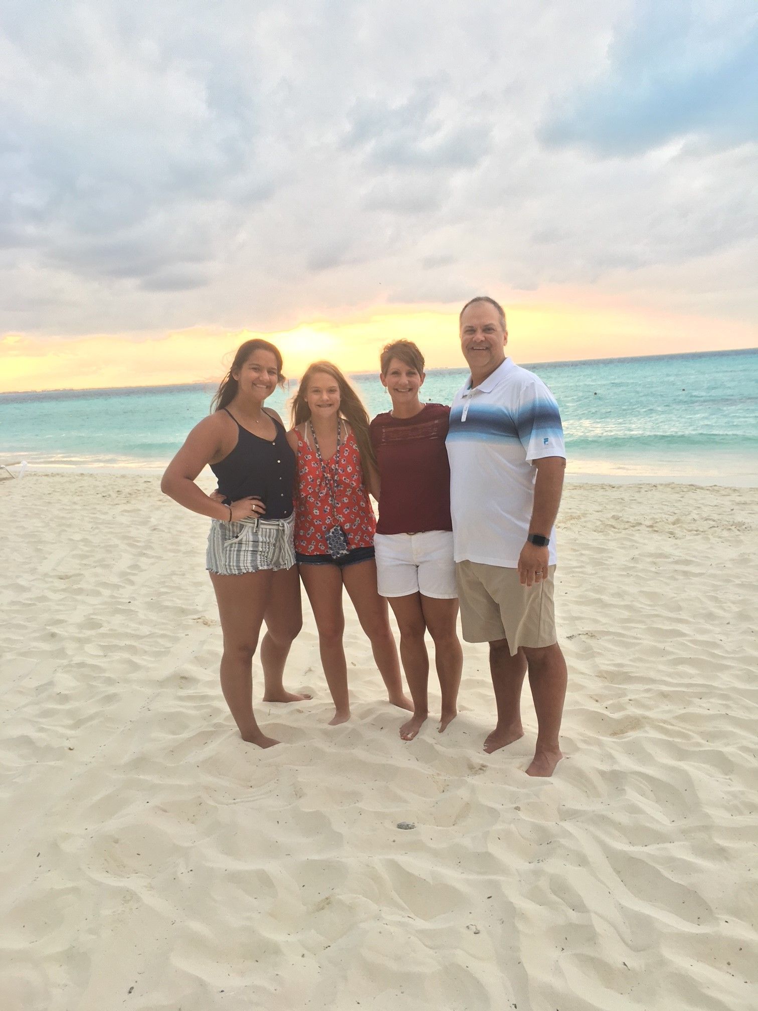 A family is posing for a picture on the beach at sunset