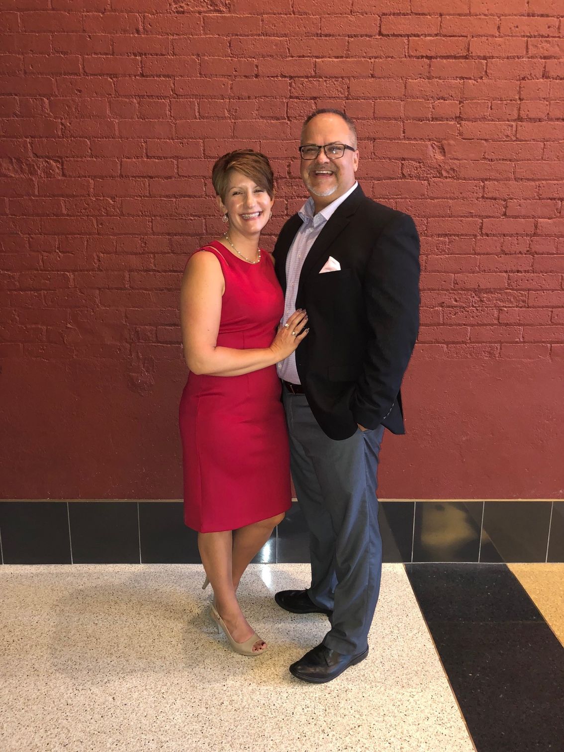 A man and a woman are posing for a picture in front of a red brick wall