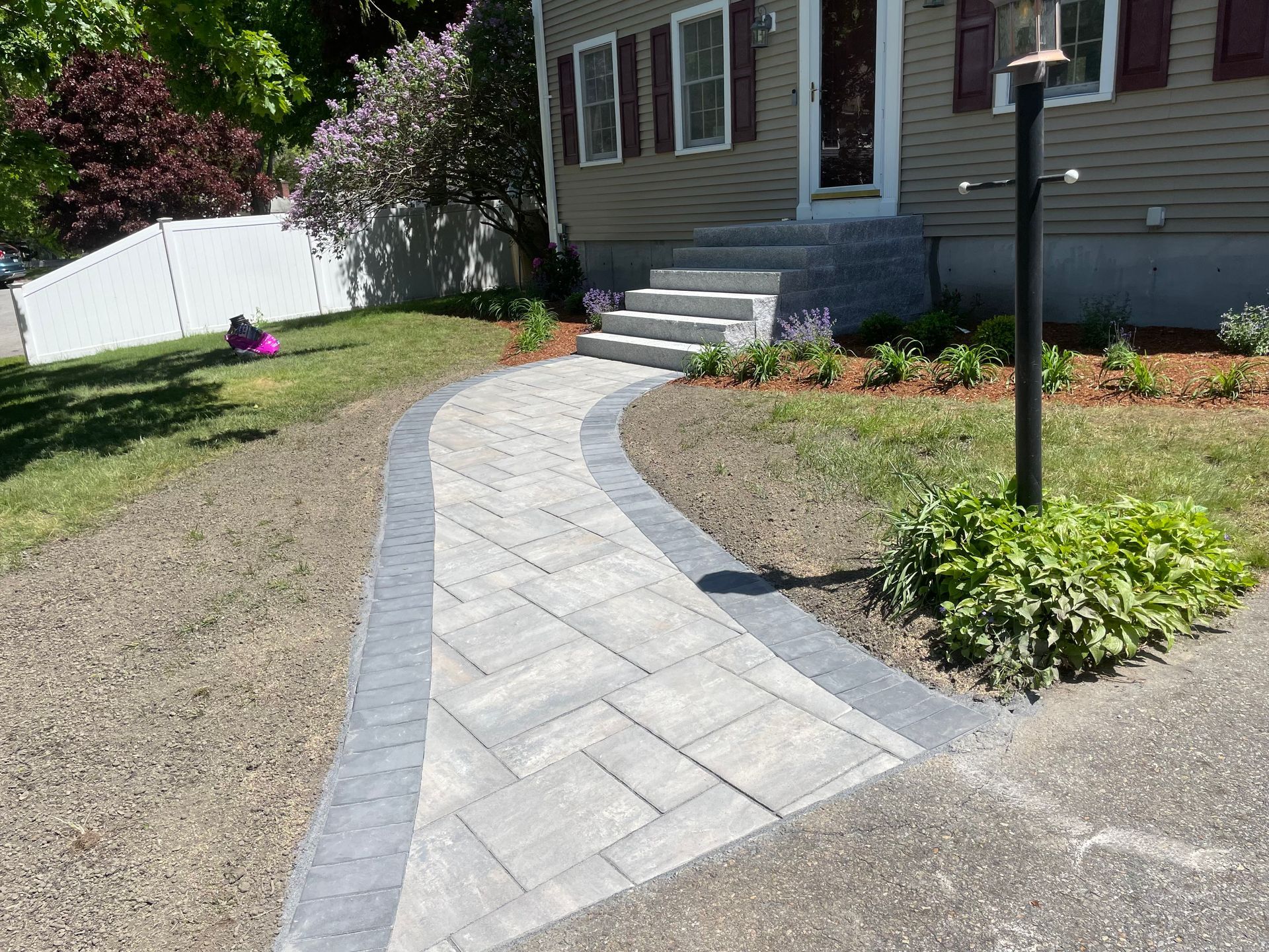 Curved stone walkway leading to a house entrance with steps, bordered by grass and flower beds