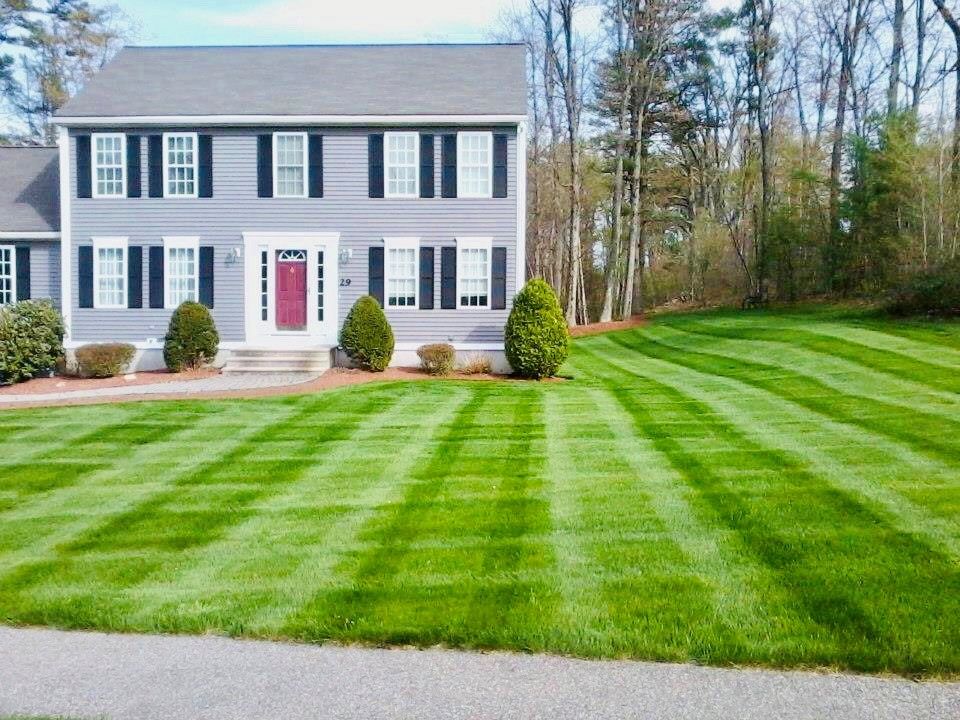 Two-story gray house with a red door and striped green lawn in front
