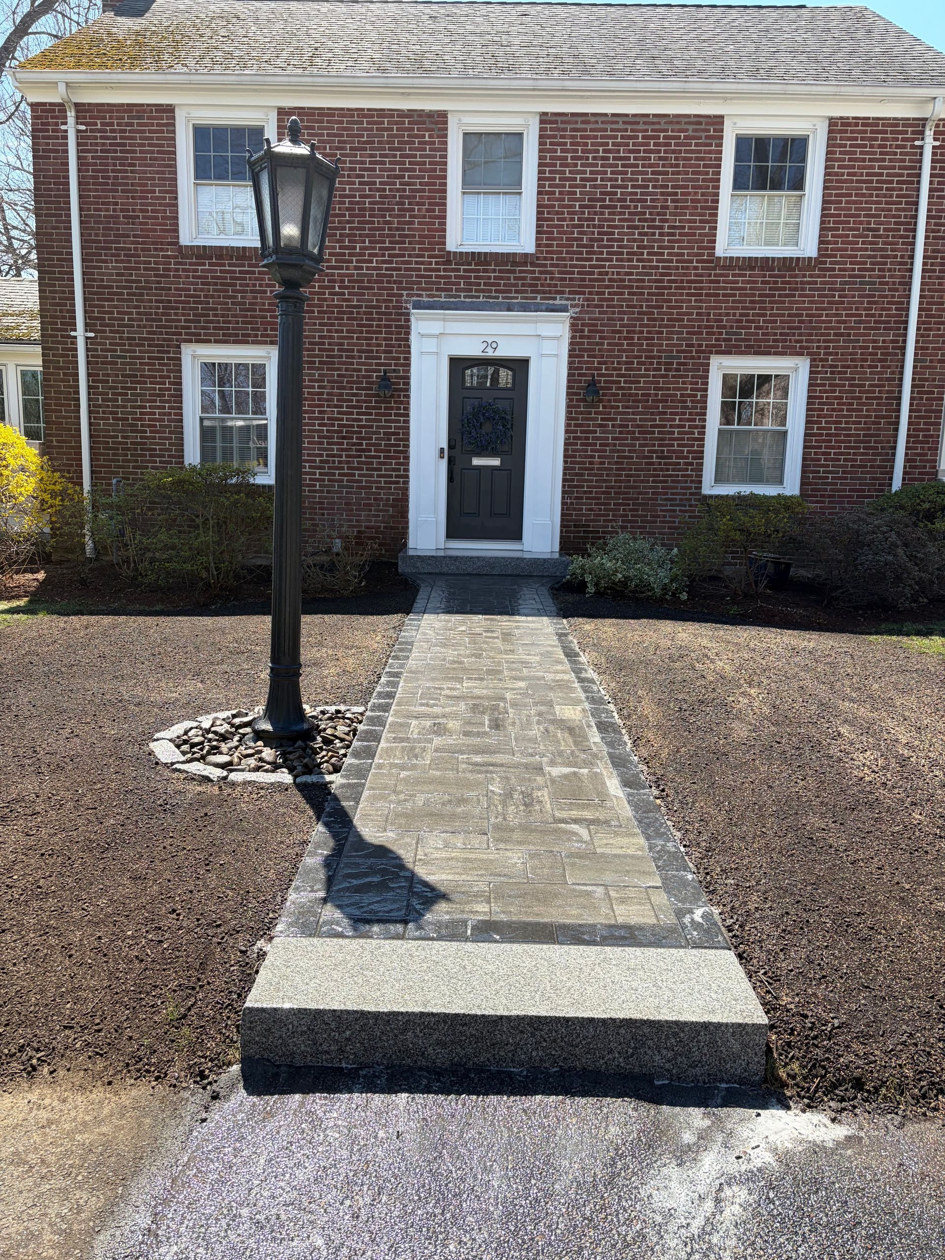Brick building entrance with stone walkway, black lamppost, and gray front door