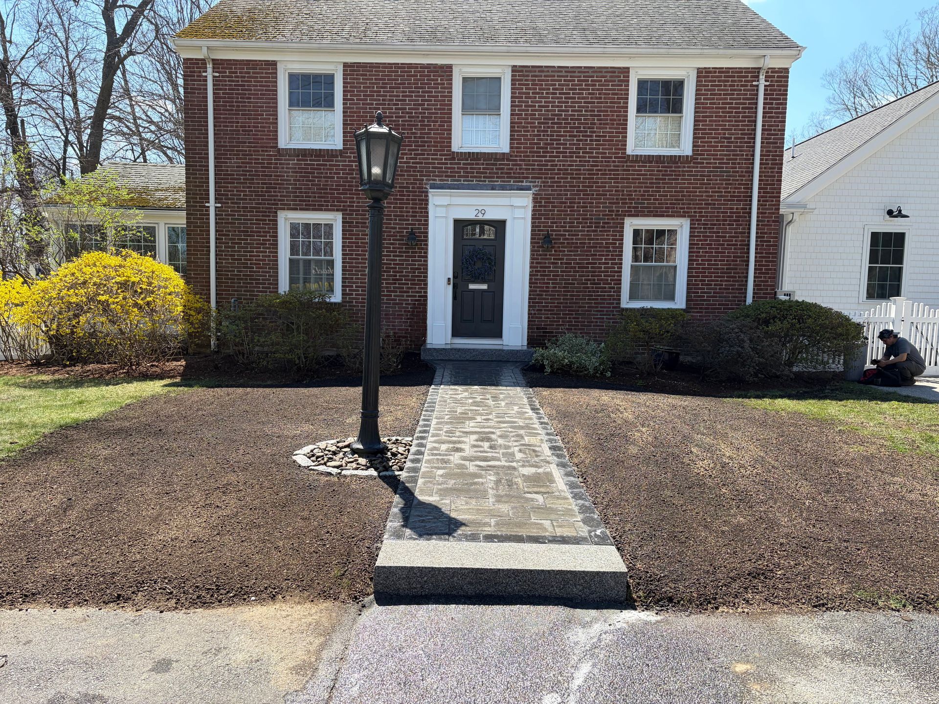 Brick house with central walkway, black lamp post, and bare winter landscaping