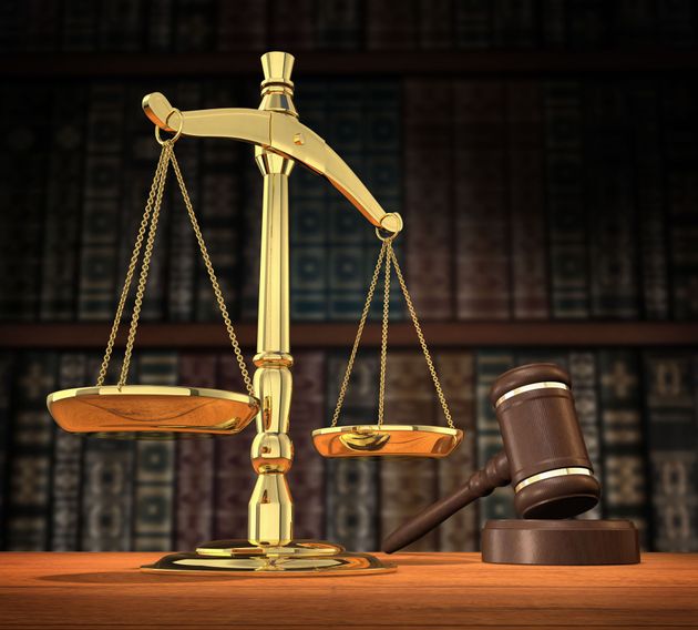 Gold justice scales beside a wooden judge’s gavel on a law library desk