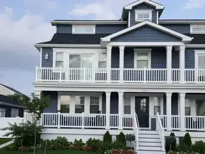 Two-story blue house with white trim, pillars, and balconies. Stairs lead to a black front door.