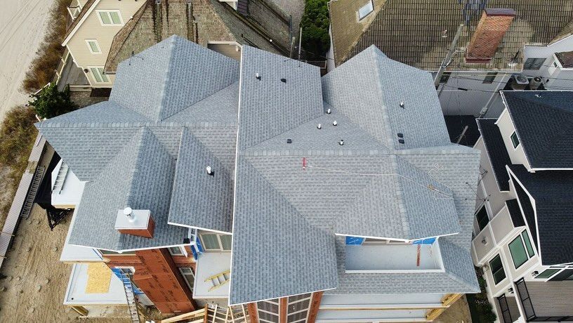 Aerial view of a house with a complex, gray shingled roof. The house is under construction and located in a residential area.