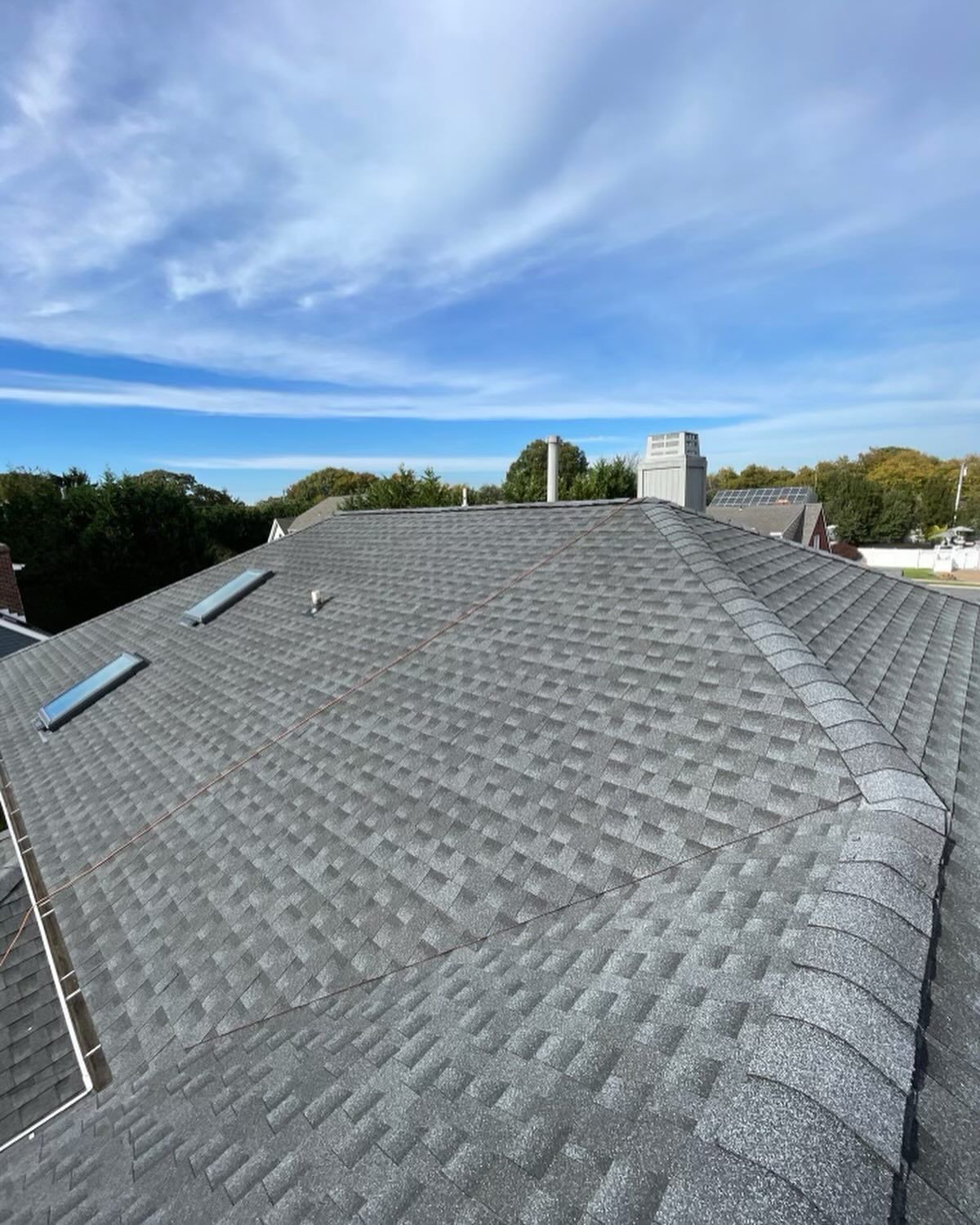 Grey asphalt shingle roof with two skylights and a chimney under a partly cloudy blue sky.