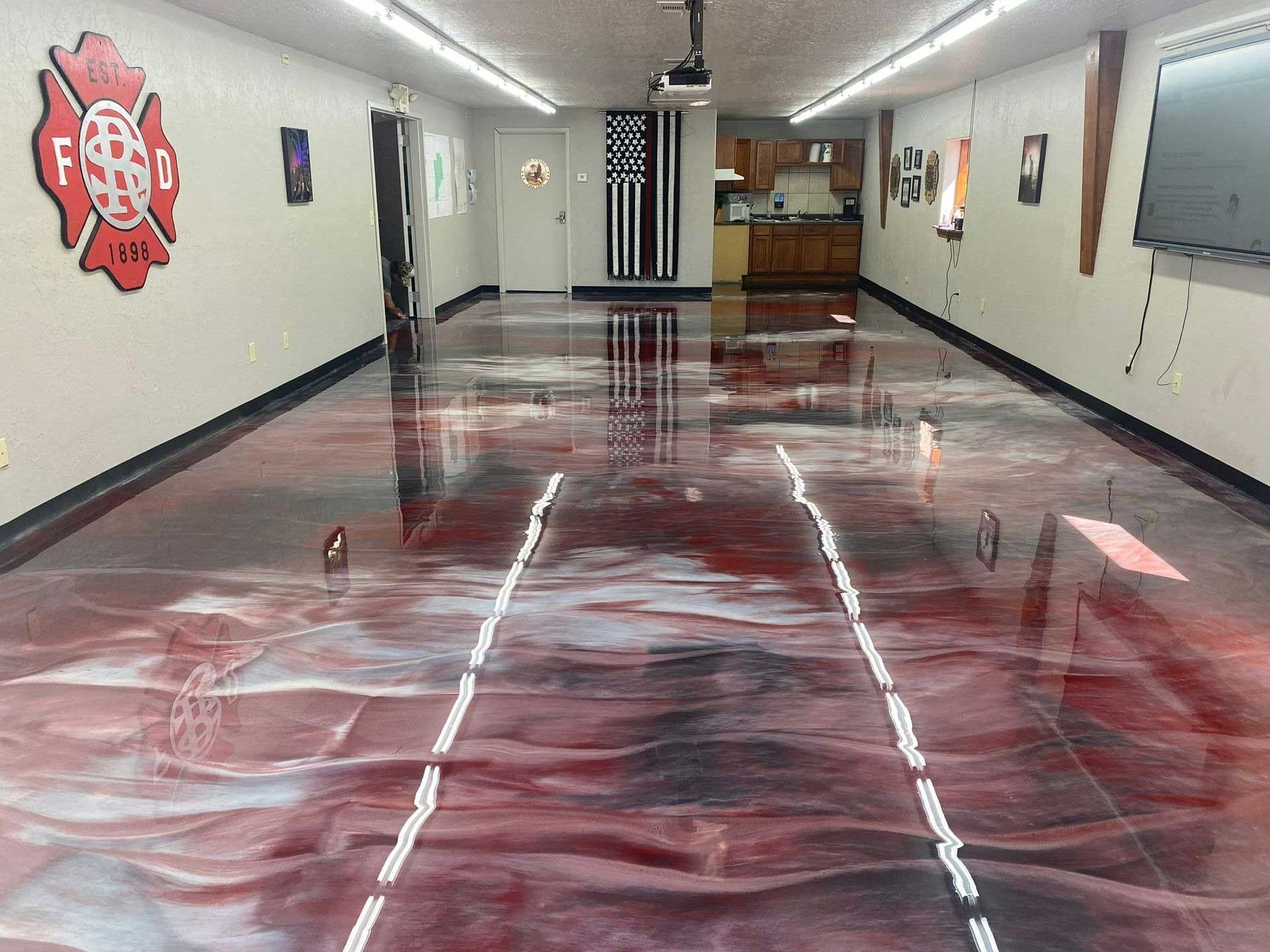 Garage with a metallic red epoxy floor and white racing stripes, a firefighter emblem, and kitchen in the back.
