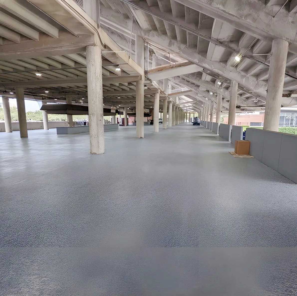 Concrete walkway under a covered structure with support columns and gray flooring.