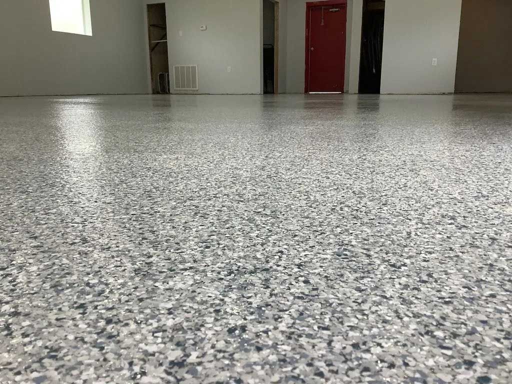 Epoxy-coated floor with speckled gray, white, and blue chips in a room with light gray walls and a red door.