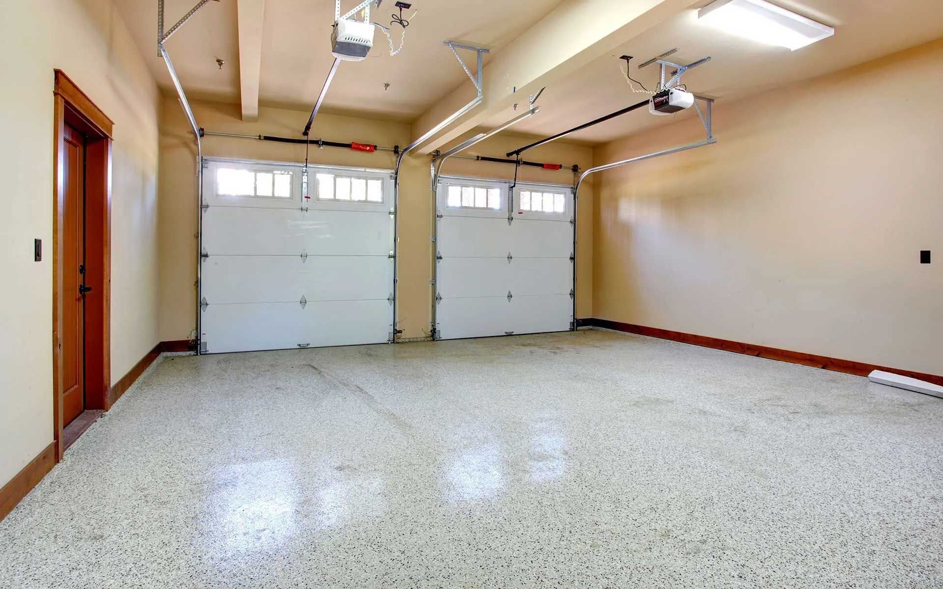 An empty garage with two closed white garage doors and a speckled floor.