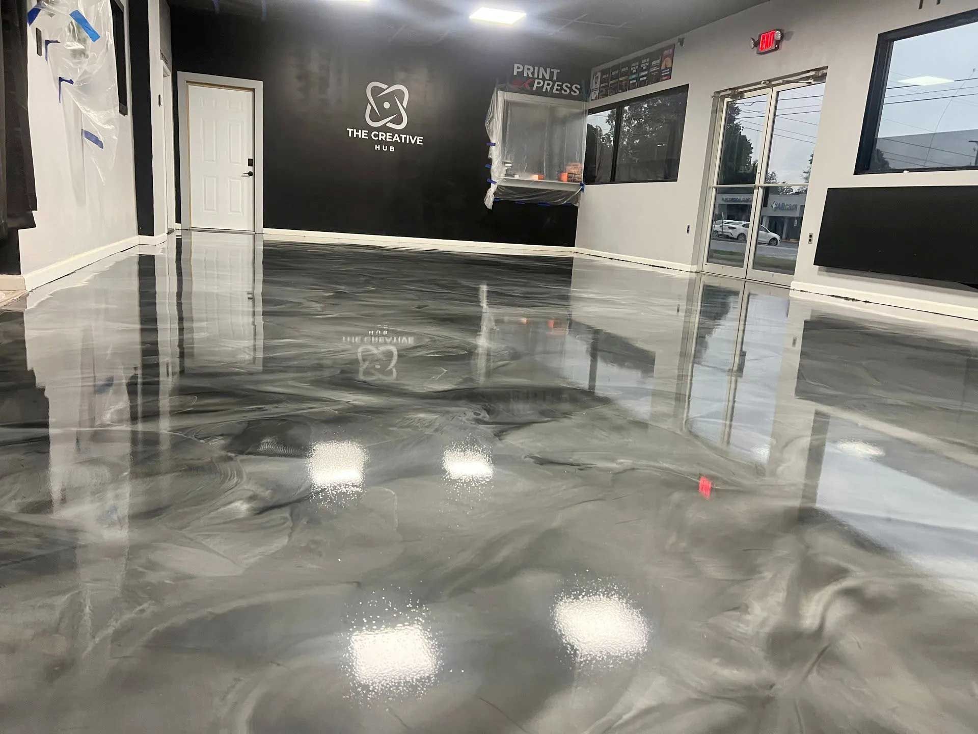 Shiny, metallic-grey epoxy floor inside a commercial space with a black accent wall and white door.