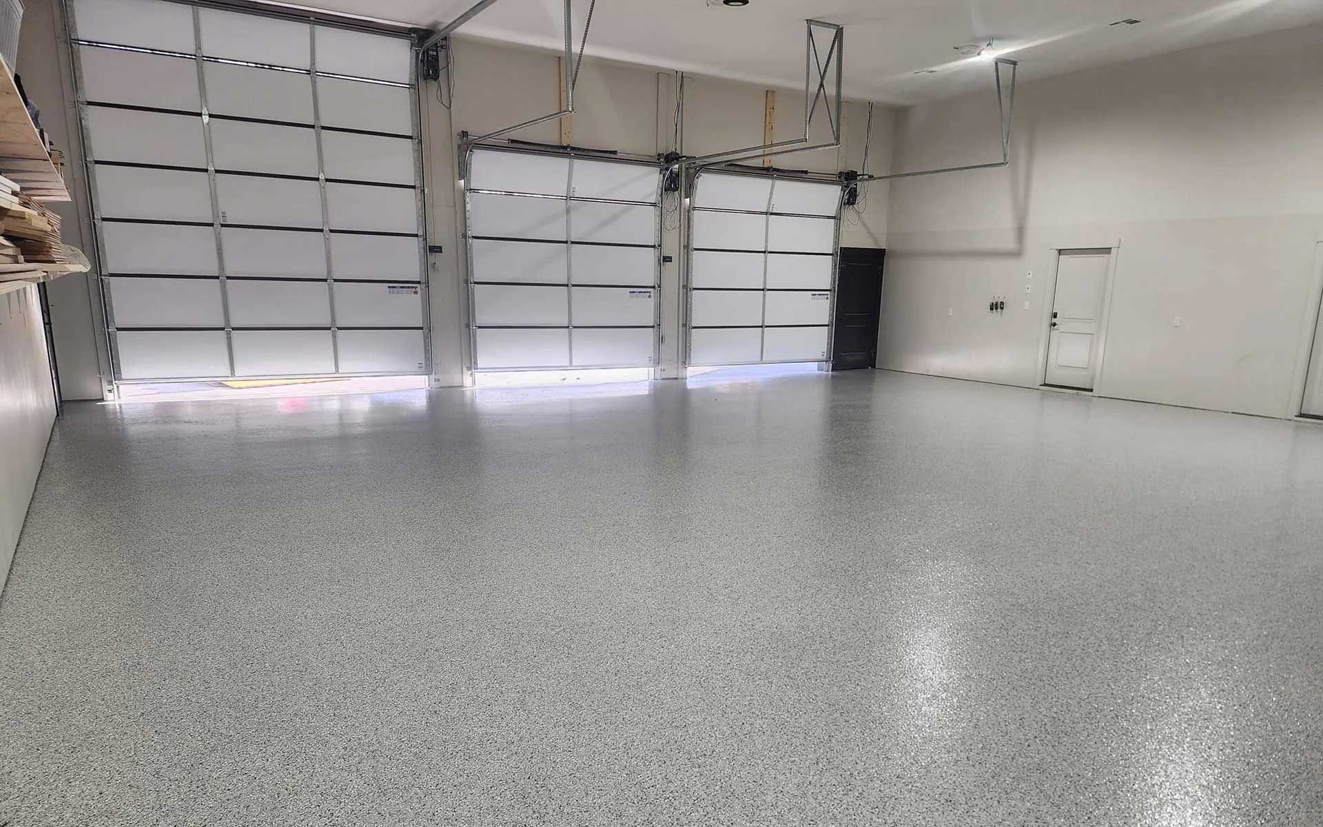 Empty warehouse interior with a gray epoxy floor and three garage doors.
