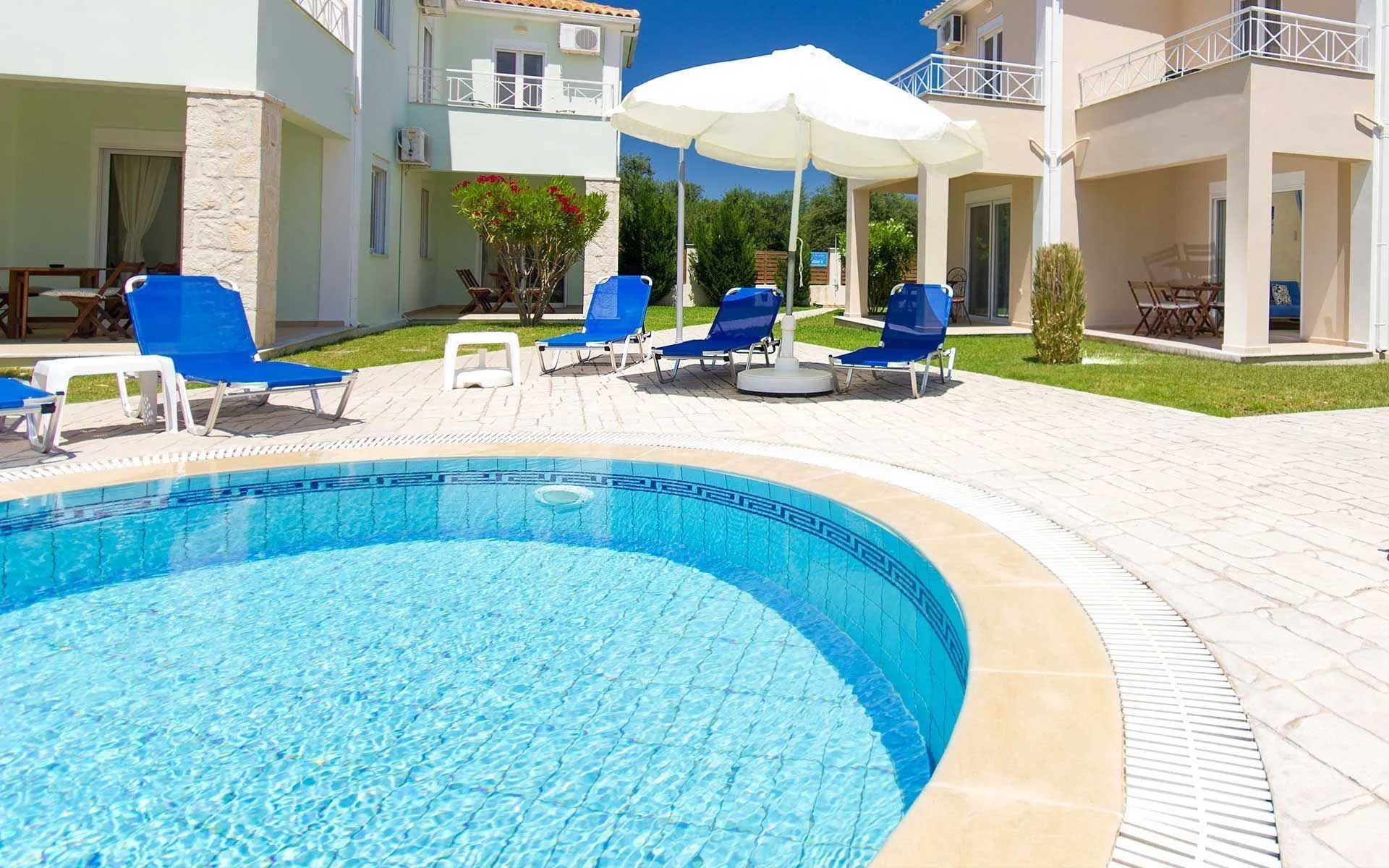 Swimming pool with lounge chairs under a white umbrella, near a building.