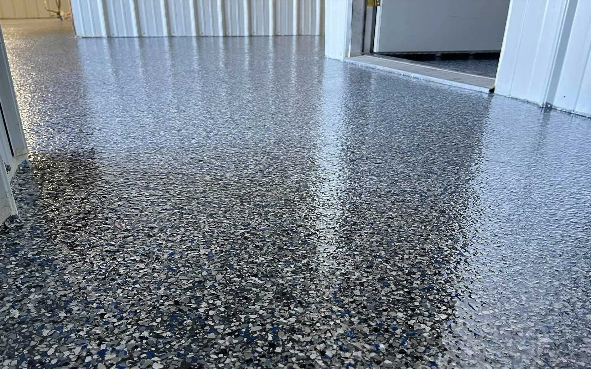 Epoxy-coated garage floor with gray and white chips. Glossy finish reflects light from the open garage door.