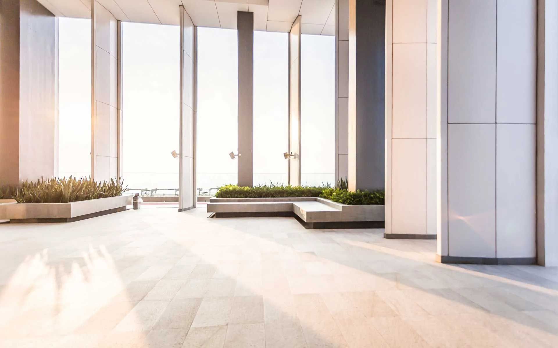 Bright, modern interior with large windows and a gray tiled floor. Planters with greenery are present.