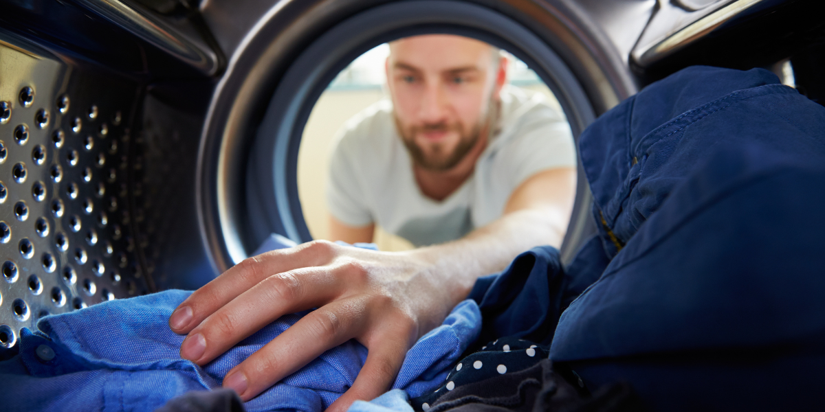 Internal view of washer drum as man pulls out laundry from it. 