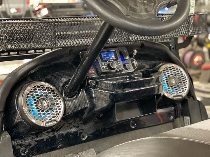 The dashboard of a golf cart with speakers and a steering wheel