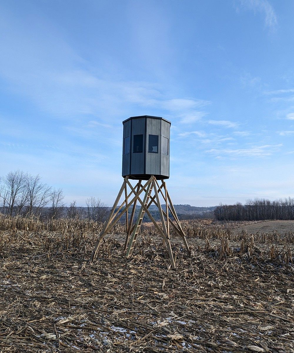 Elevated hunting blind in a harvested field under a blue sky.