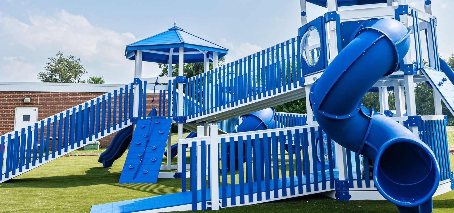 Blue and white playground on green grass under a partly cloudy sky.