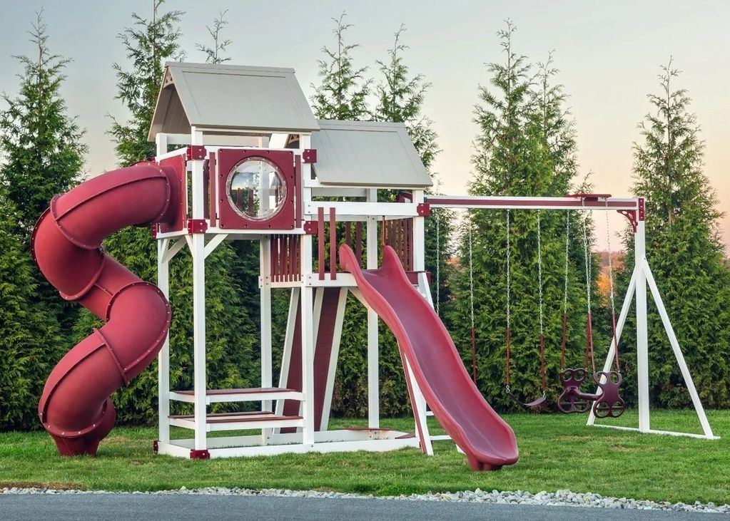 Playground with a red spiral slide, a straight red slide, and a swing set on a green lawn.