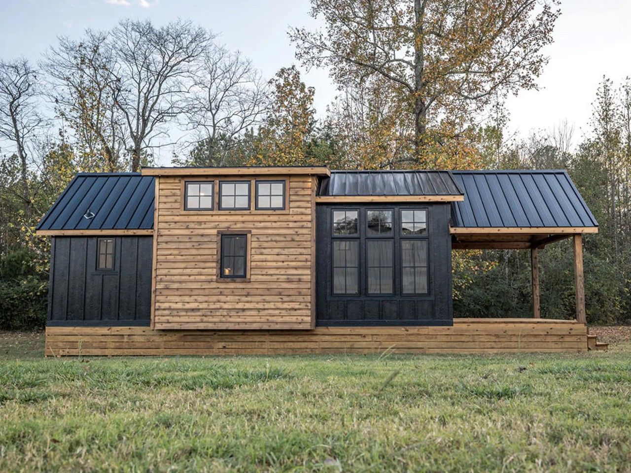 Tiny house with a black metal roof and wood siding in a grassy field.