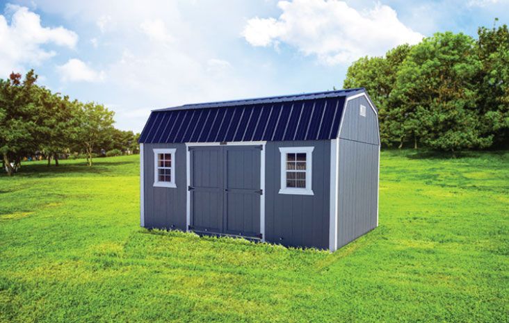 Blue storage shed with barn roof, white window trim, and double doors on green grassy field.