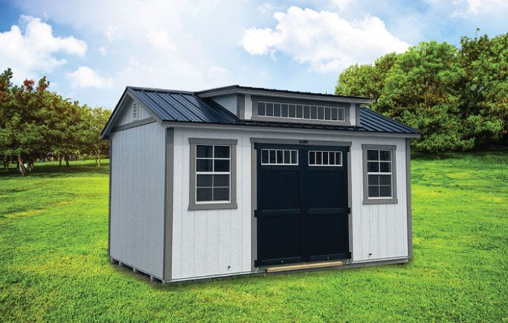 White shed with a dark blue door and blue roof on a green lawn, trees in the background.