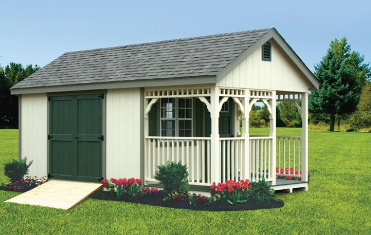 White and green shed with porch, ramp, and flower bed in a grassy yard.