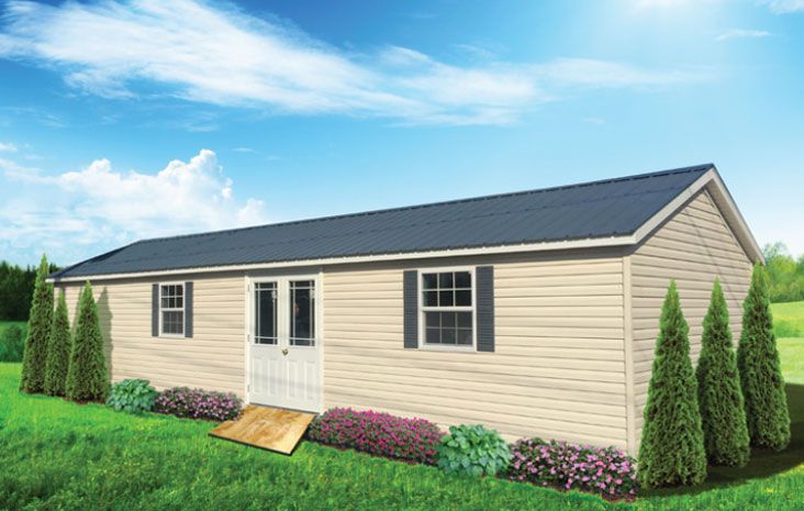 Beige shed with black roof, door with ramp, two windows, and landscaping.