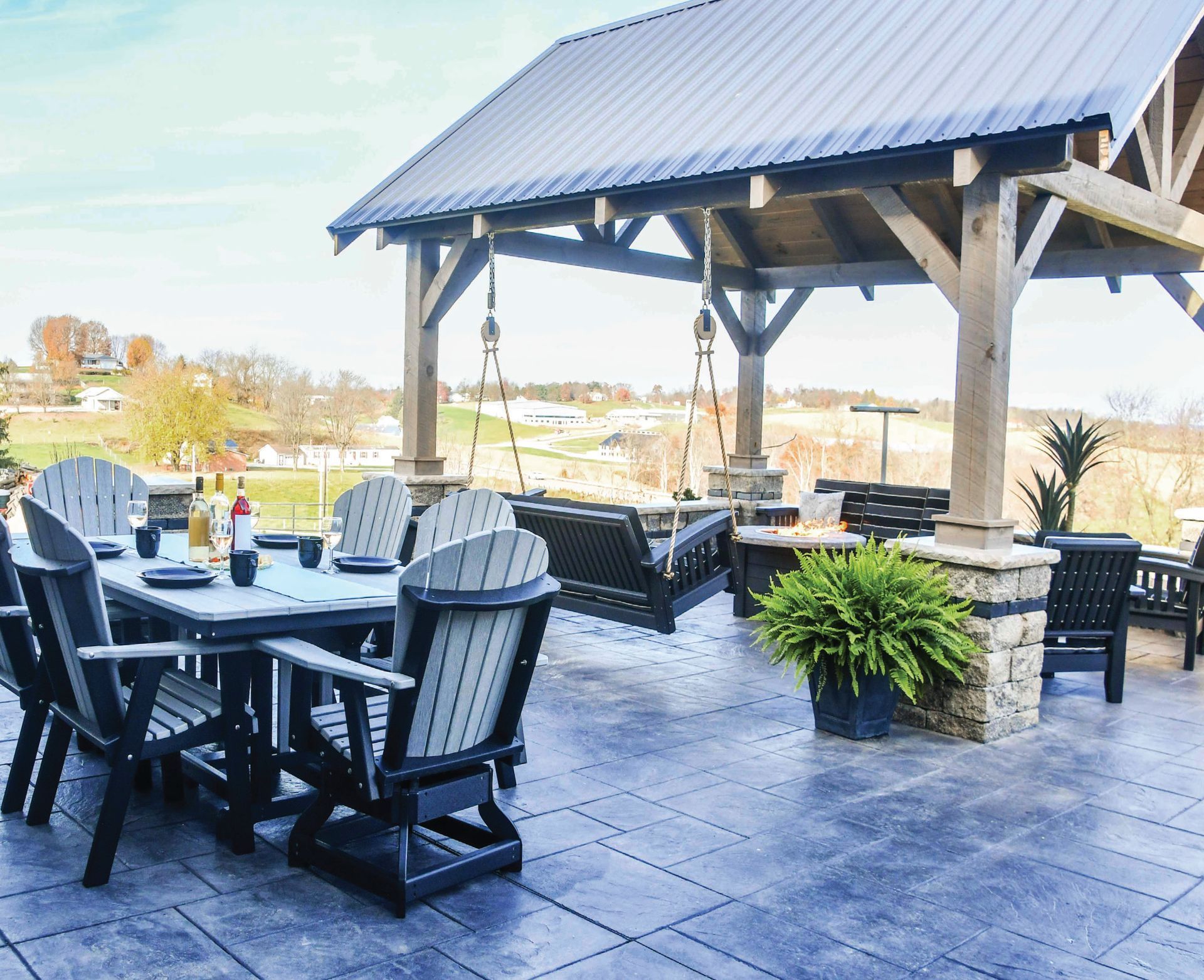 Patio with dining set, swing, and pergola overlooking a rural landscape.