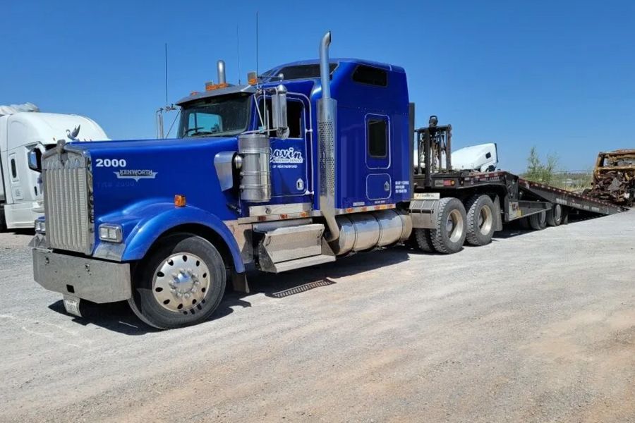 A blue semi truck with a flatbed trailer is parked on the side of the road.